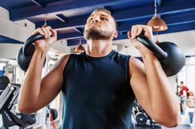 Yakışıklı, güçlü bir adam su ısıtıcılarıyla egzersiz yapıyor.