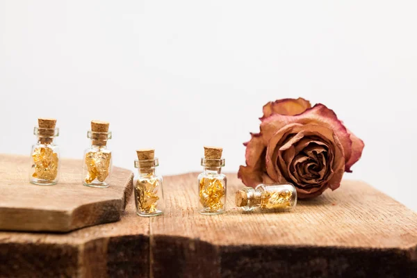 Still life composition with small glass bottles with golden paper inside and dried rose — Stock Photo, Image