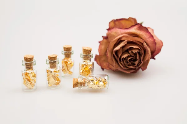 Stillleben-Komposition mit kleinen Glasflaschen mit goldenem Papier innen und getrockneter Rose — Stockfoto