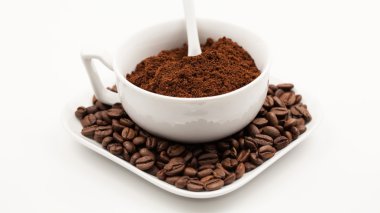 Beyaz kahve kupa, kahve plaka ve çay kaşığı kahve çekirdekleri ve kahve tozu ile