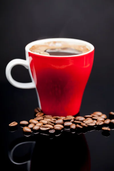 Красная чашка кофе с кофейными зернами и темным фоном — стоковое фото
