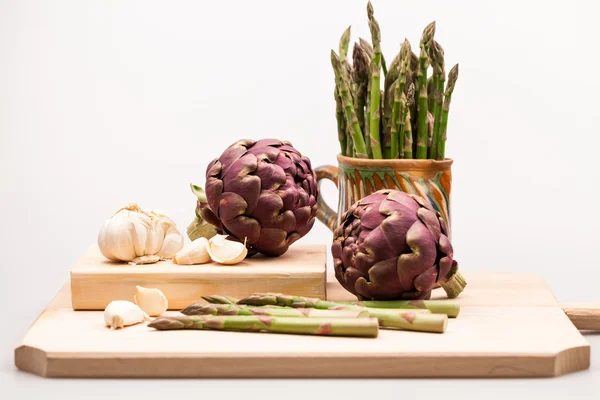 Artichokes, asparagus stems and garlic on a wooden kitchen board — Stock Photo, Image
