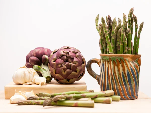Artichokes, asparagus stems and garlic on a wooden kitchen board — Stock Photo, Image