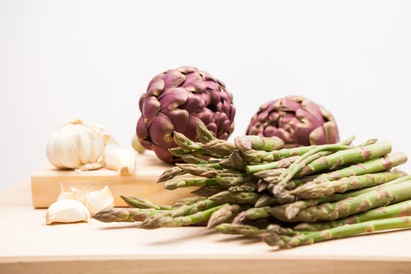 Carciofi, asparagi e aglio su una tavola da cucina in legno — Foto Stock