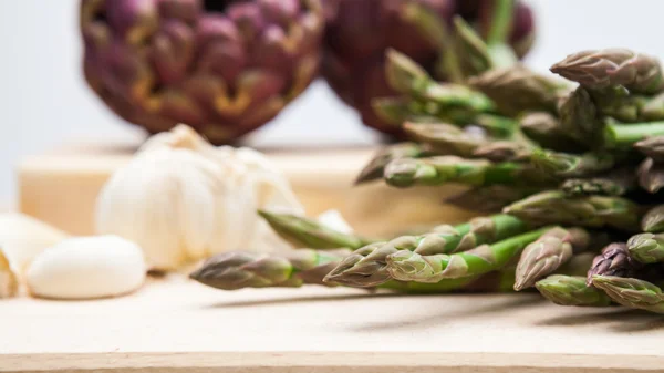 Artichokes, asparagus stems and garlic on a wooden kitchen board — Stock Photo, Image