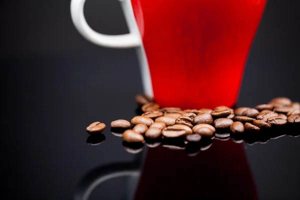 Xícara de café vermelho com grãos de café e fundo escuro — Fotografia de Stock