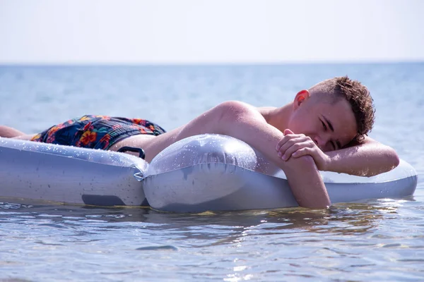 The guy swims on a mattress in the sea.