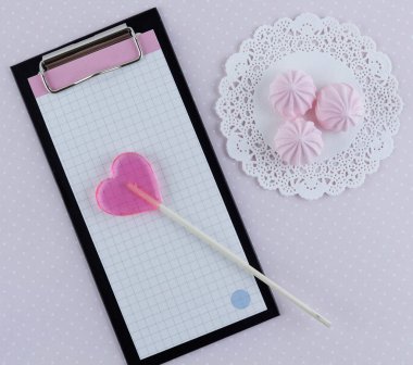 Not defteri. Pembe kalp şeklinde bir lolipop ve üç tane de pembe lokum..