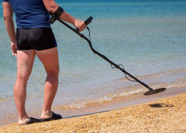 Metal detektör bobini ve denizin arka planında hazine arayan bir adamın bacakları..