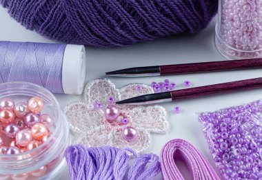 Leylak rengi iplikler, boncuklar, boncuklar, dikiş iplikleri, örgü iğneleri, kurdeleler.