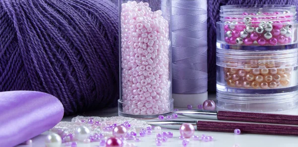 Leylak rengi iplikler, boncuklar, boncuklar, dikiş iplikleri, örgü iğneleri, kurdeleler.