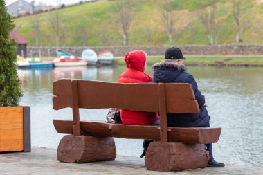 Yaşlı bir adam ve kadın gölün kenarındaki bankta oturuyorlar.