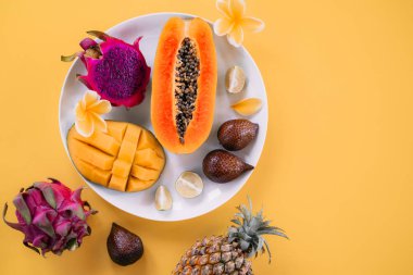 Sarı arka planda Papaya, mango, ejderha meyvesi ve limon tabağı.