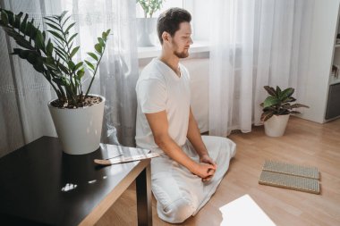 Genç adam meditasyon yapıyor, lotus pozisyonunda oturuyor..