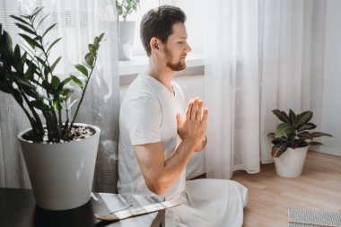 Genç adam meditasyon yapıyor, lotus pozisyonunda oturuyor..