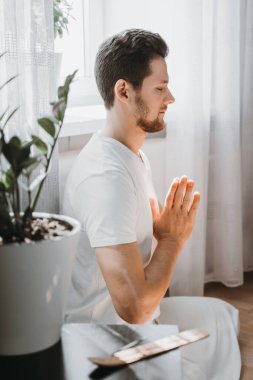 Genç adam meditasyon yapıyor, lotus pozisyonunda oturuyor..