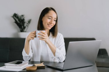 Genç bir kadın masada oturuyor ve dizüstü bilgisayar kullanıyor..