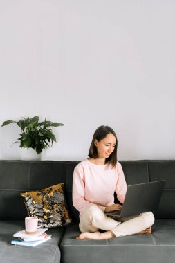 Kanepede oturan ve dizüstü bilgisayar kullanan genç bir kadın..