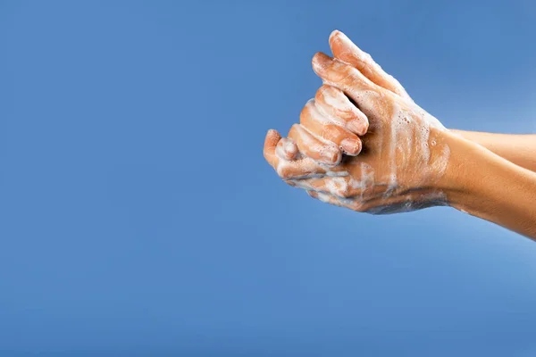 Wash your hand - coronavirus healthcare and hygiene concept. Photo of woman hands with soap foam on blue background.