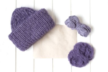 Beyaz arka planda örülmüş mor şapka. Yünlü mor iplik topları. Üst Manzara. Düz plan. Dilek listesi. Metin ve tasarım için yer. Boşluğu kopyala.