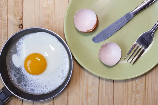 Drewniany stół ze smażonym jajkiem, skorupkami jaj, nożem i widelcem. — Zdjęcie stockowe