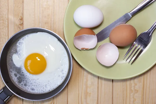Drewniany stół ze smażonym jajkiem, skorupkami jaj, nożem i widelcem. — Zdjęcie stockowe
