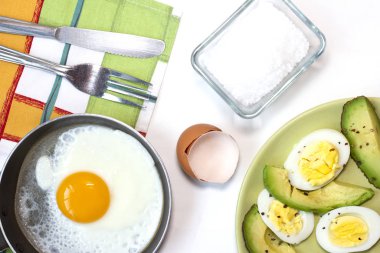 Tavada yumurta, haşlanmış yumurta ve kaçınma ile yeşil tabak, mutfak havlusu, çatal ve bıçak beyaz masada.