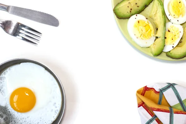 Fried egg on the pan, green plate with boiled egg and avoado, kitchen towel, fork on the white table — 스톡 사진