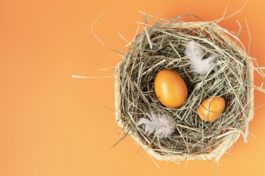 Turuncu arka plandaki hasır sepette turuncu yumurtalar. Uzayı kopyala Metin ve tasarım için yer. Mutlu Paskalyalar. Üst Manzara. Düz Düzen.