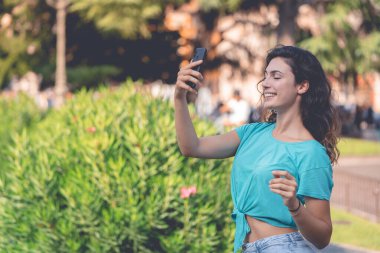 Gülümseyen kız yeşil bitkilerin arkasında kendisiyle selfie çekiyor.