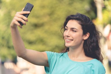 Gülümseyen kız yeşil bitkilerin arkasında kendisiyle selfie çekiyor.