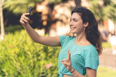 Gülümseyen kız yeşil bitkilerin arkasında kendisiyle selfie çekiyor.