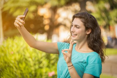 Gülümseyen kız yeşil bitkilerin arkasında kendisiyle selfie çekiyor.