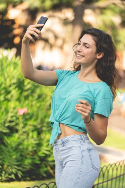 Gülümseyen kız yeşil bitkilerin arkasında kendisiyle selfie çekiyor.