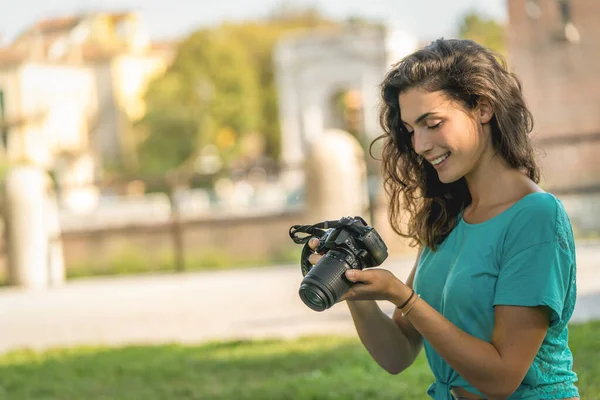 Fotograaf meisje zitten op het gras kijken naar de camera scherm, glimlachend — Stockfoto