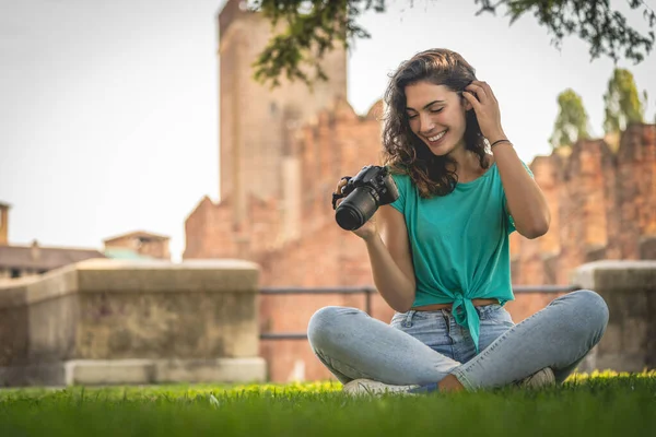Fényképész lány ül a füvön nézi a kamera képernyőjén, mosolyogva — Stock Fotó