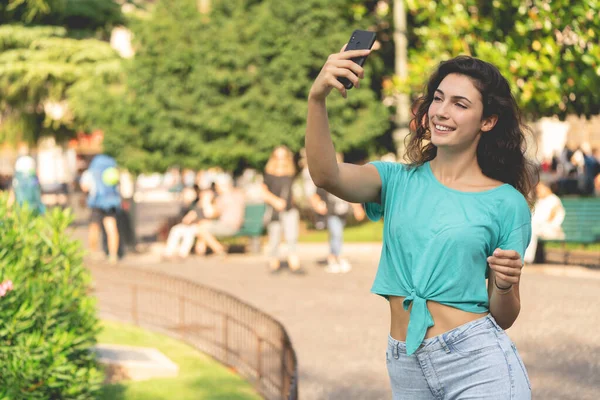 Glimlachend meisje het nemen van een selfie met zichzelf achter van groene planten — Stockfoto