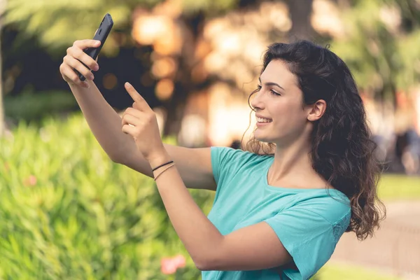 Glimlachend meisje het nemen van een selfie met zichzelf achter van groene planten — Stockfoto