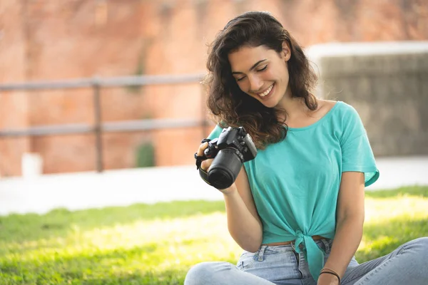 Fotograaf meisje zitten op het gras kijken naar de camera scherm, glimlachend — Stockfoto