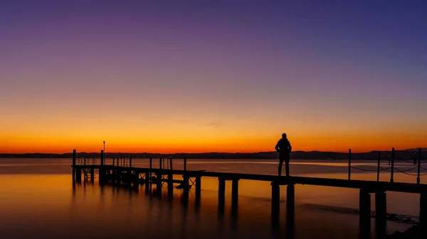 Egy férfi sziluett áll a fából készült mólón magányos a tengernél gyönyörű naplementével. naplemente tengerpart egy fából készült mólónál. Jogdíjmentes Stock Képek