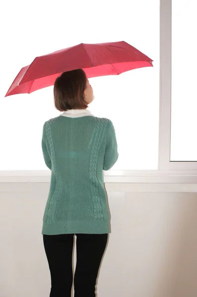 The girl with the red umbrella and the sweater looks out of the window