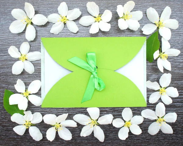 Gift envelope with green ribbon on wooden background with real flowers Apple