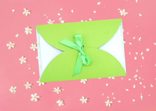 Gift envelope with green ribbon on a pink background with flowers