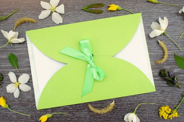 Gift envelope with green ribbon on floral wooden background. Flat lay