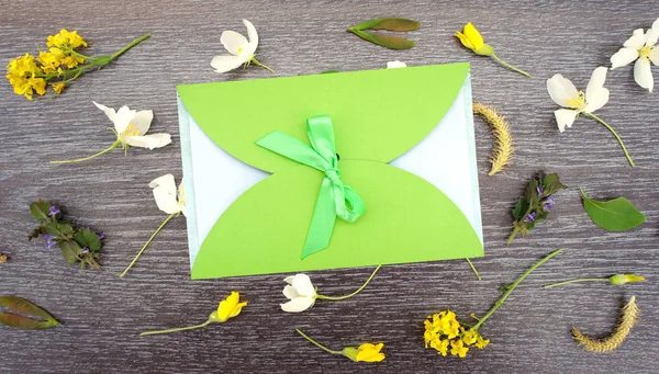Gift envelope with green ribbon on floral wooden background. Flat lay