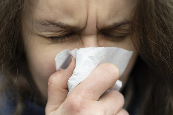 Sick young caucasian woman blowing her nose in a handkerchief standing on the street on cold weather. Unhappy girl suffering from runny nose, colds and flu, fever, coronavirus symptoms. 2019-ncov.