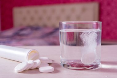 Ateşli tablet bir bardak suda çözünür. Masada bir avuç dolusu hap var. Yatak odasındaki yatağın arka planı bulanık. Virüs hastalıklarının tedavisi. Depresyon ve uykusuzluk için yardım