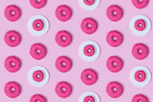 Whole round pink doughnuts on a white plate. Seamless background. Bright sweet buns. Colorful design for textiles, Wallpaper, fabric, decor. Fashionable solar pattern. Minimal summer concept. Flat lay