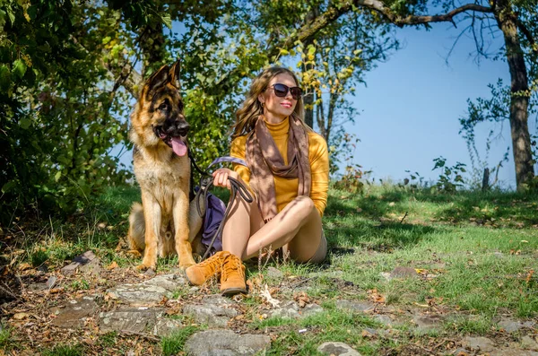 Glückliches Mädchen, das mit einem Schäferhund der Hunderasse im Park sitzt und lächelnd in die Ferne blickt. ein junger pubertärer Welpe, treuer Freund und Wächter. auf dem gelb-grünen Herbsthintergrund der Bäume — Stockfoto