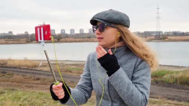 Het meisje blogger is live streaming online op de telefoon, maar het geluid verdwijnt in de hoofdtelefoon. technisch probleem. Een vrouw in een jas buiten, pratend en lachend. Technologie en leefstijlconcept. — Stockvideo